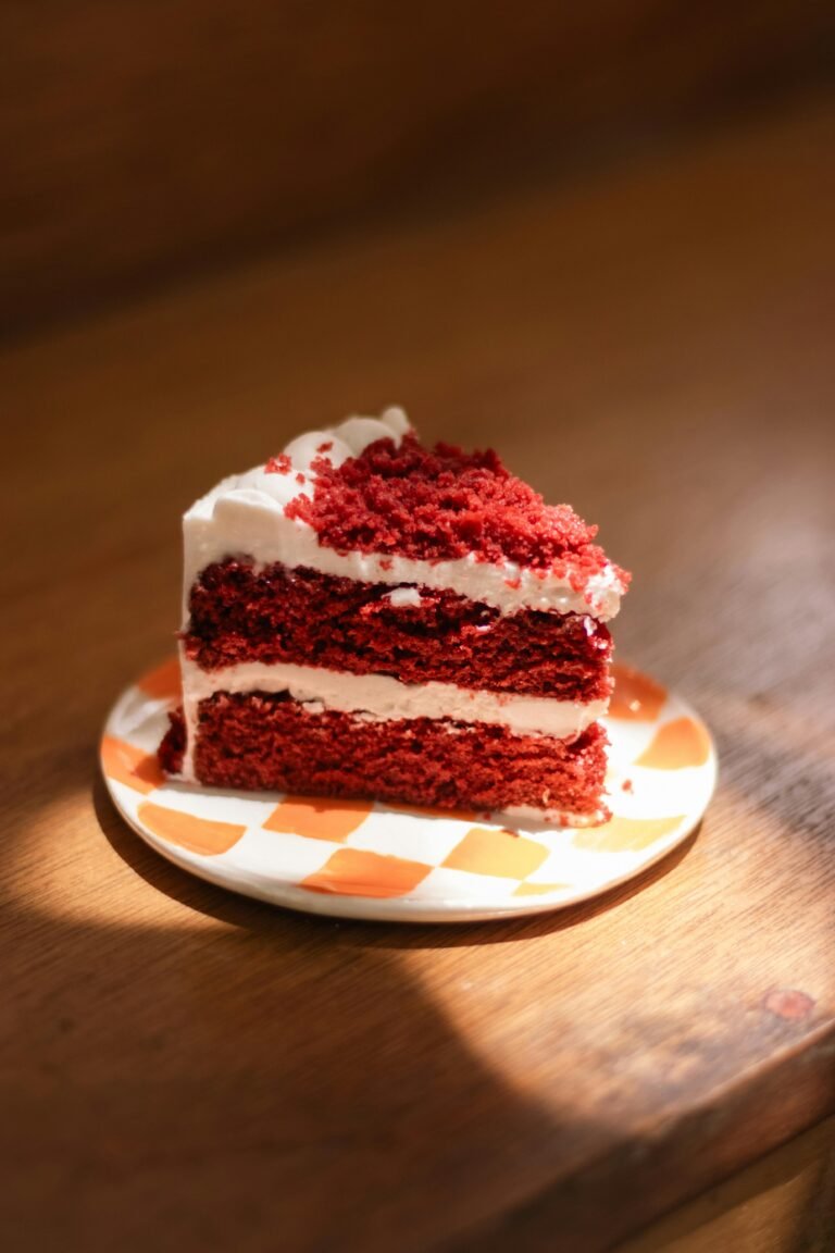 Delicious slice of red velvet cake with cream cheese frosting on a colorful plate.